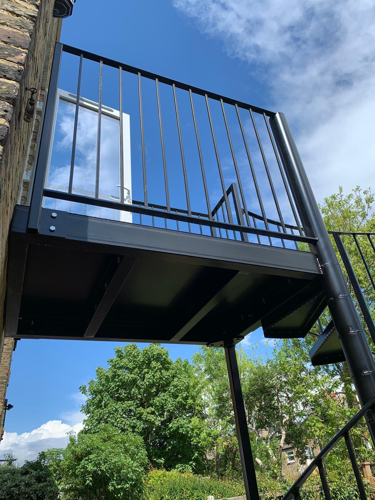 Yellow brick house: bolt-on balcony in black with upright bars, spiral down to the garden