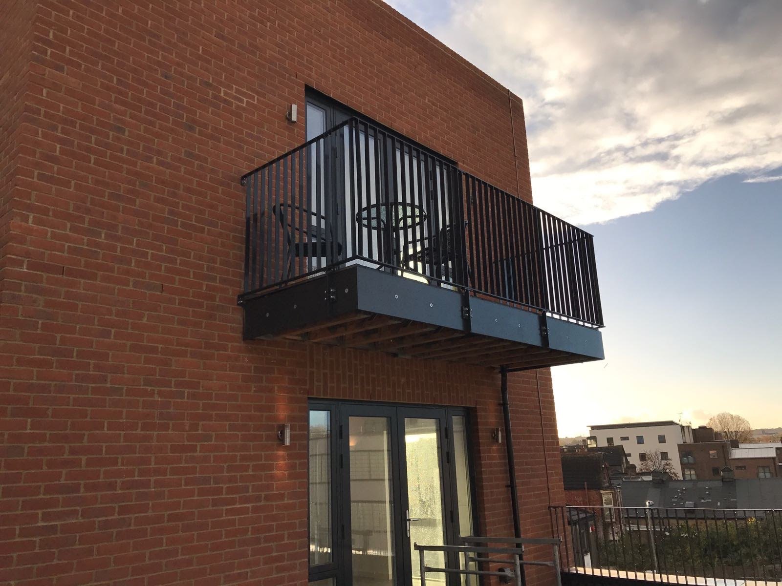 Red brick flats at dusk: projecting balcony in black, upright bar guarding