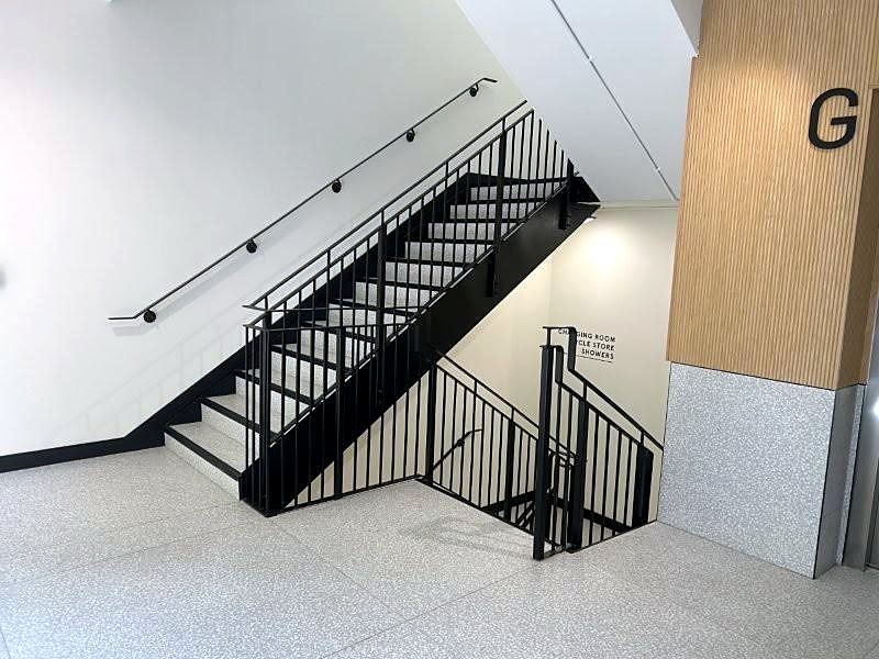 Black dog-leg stair turning up a stairwell, upright bars on the open side and a rail on the wall
