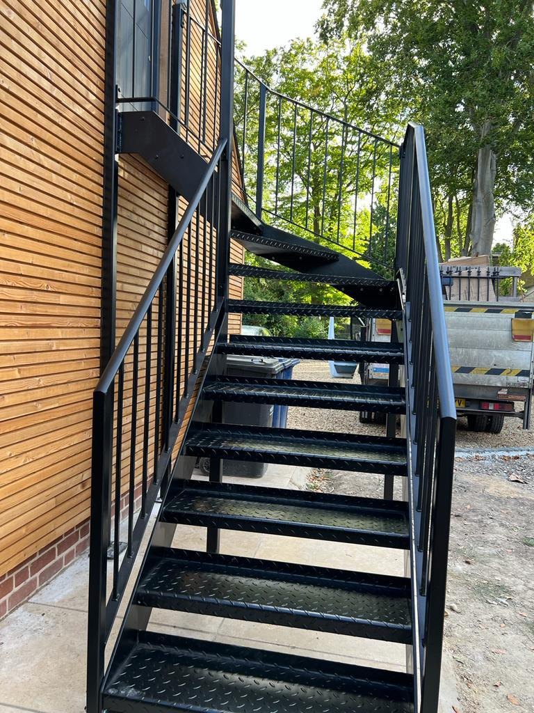 Clad barn conversion: black outdoor flight climbing to a first-floor landing
