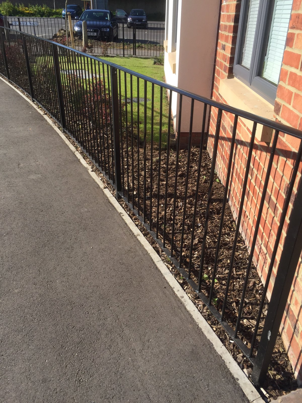Pavement edge: run of black upright-bar railing in front of a planted border