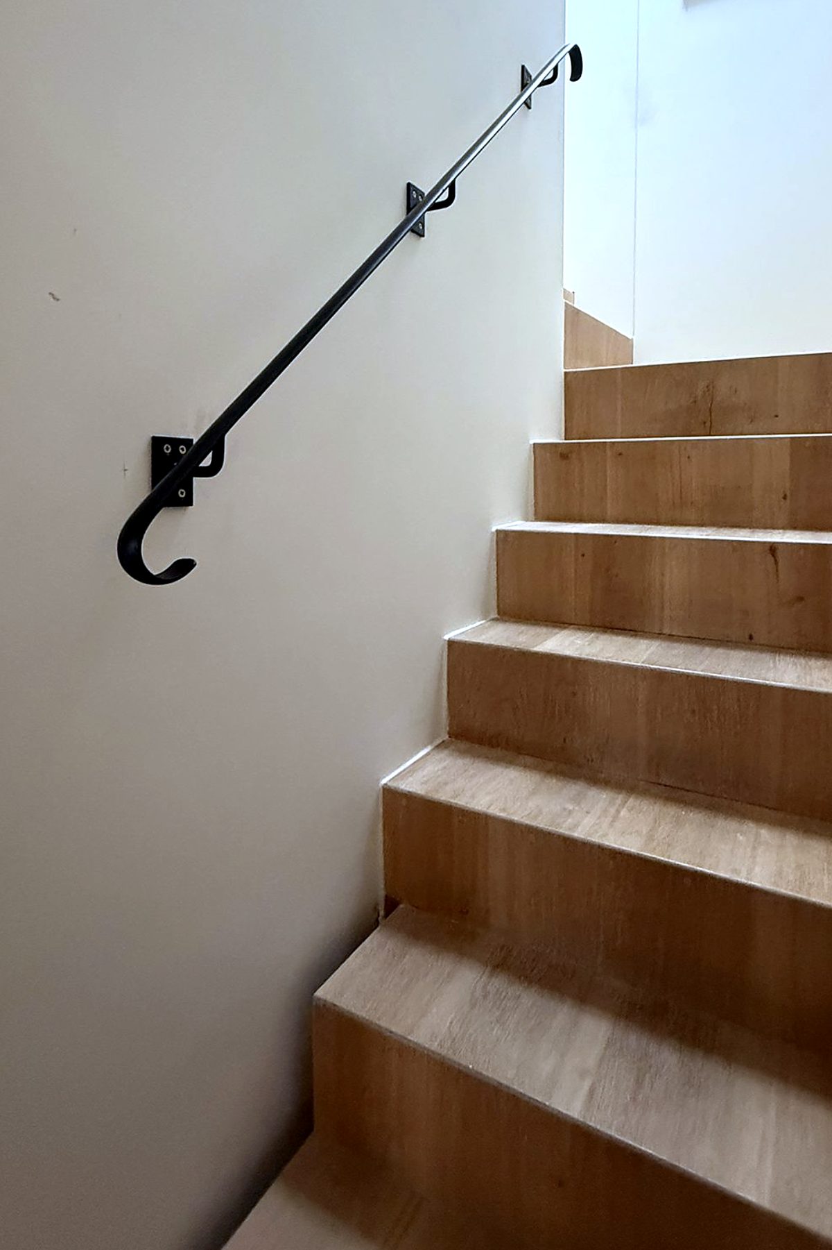 Black steel wall-mounted handrail with a hooked end beside an oak staircase