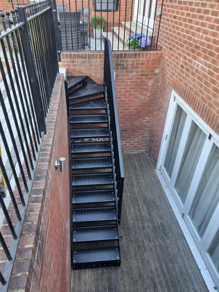 Looking down a lightwell: black winder flight on durbar treads to a decked basement court