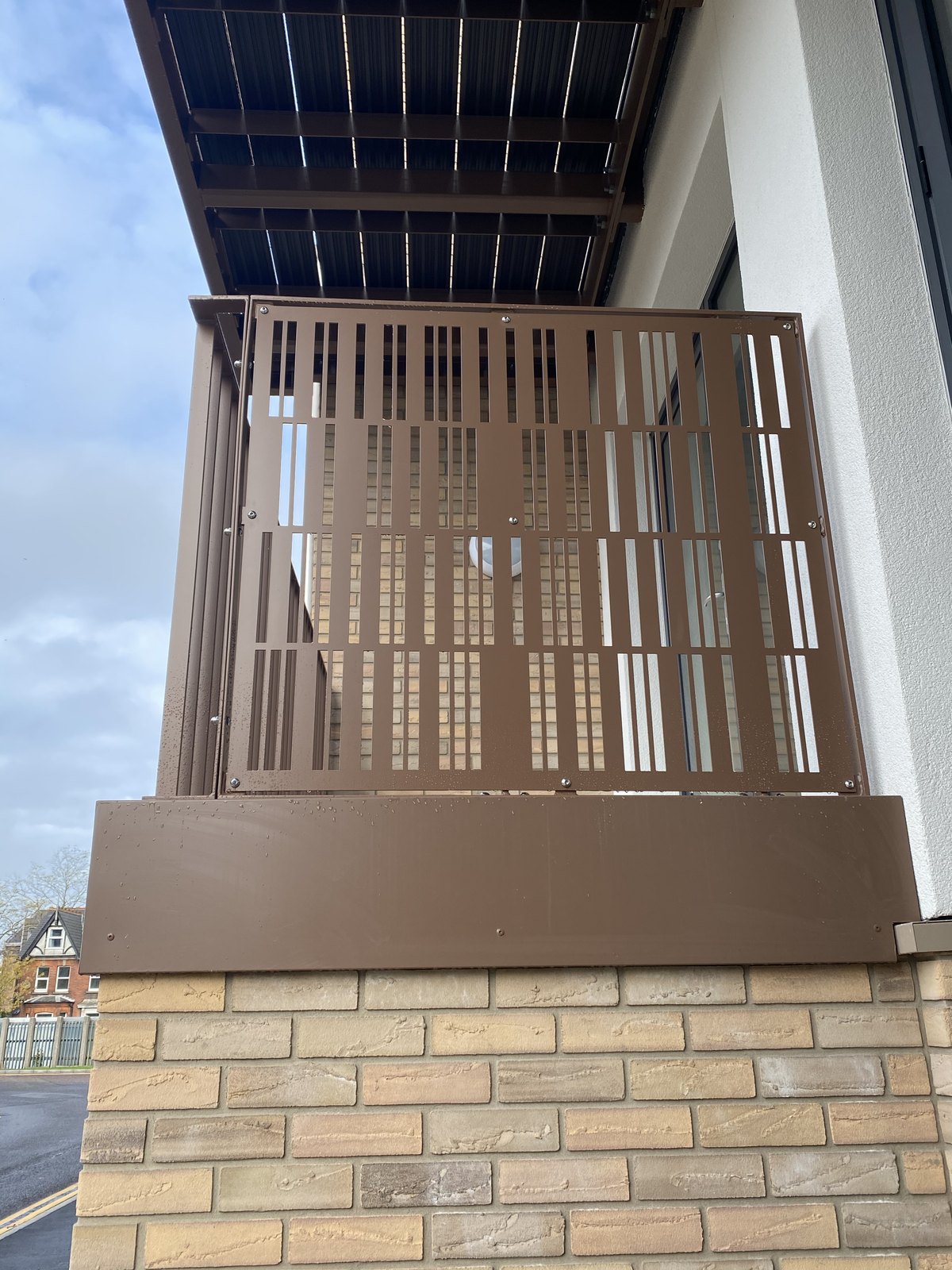 New-build flat: balcony guarding in bronze laser-cut sheet above a plain fascia