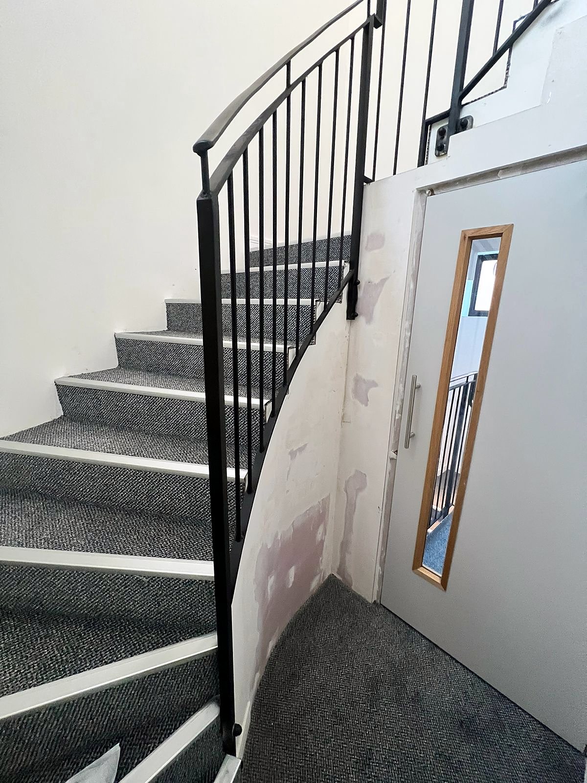 Carpeted curved stair with black steel bars following the sweep of the flight