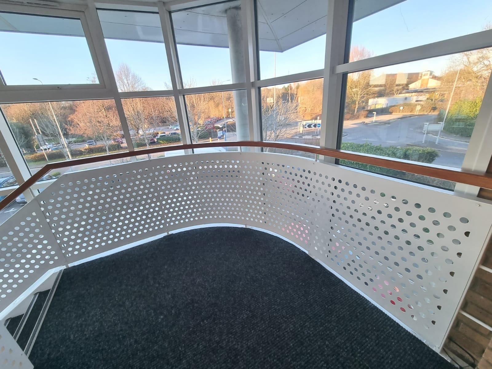 Glazed office landing: curved guarding in white punched sheet under a hardwood rail
