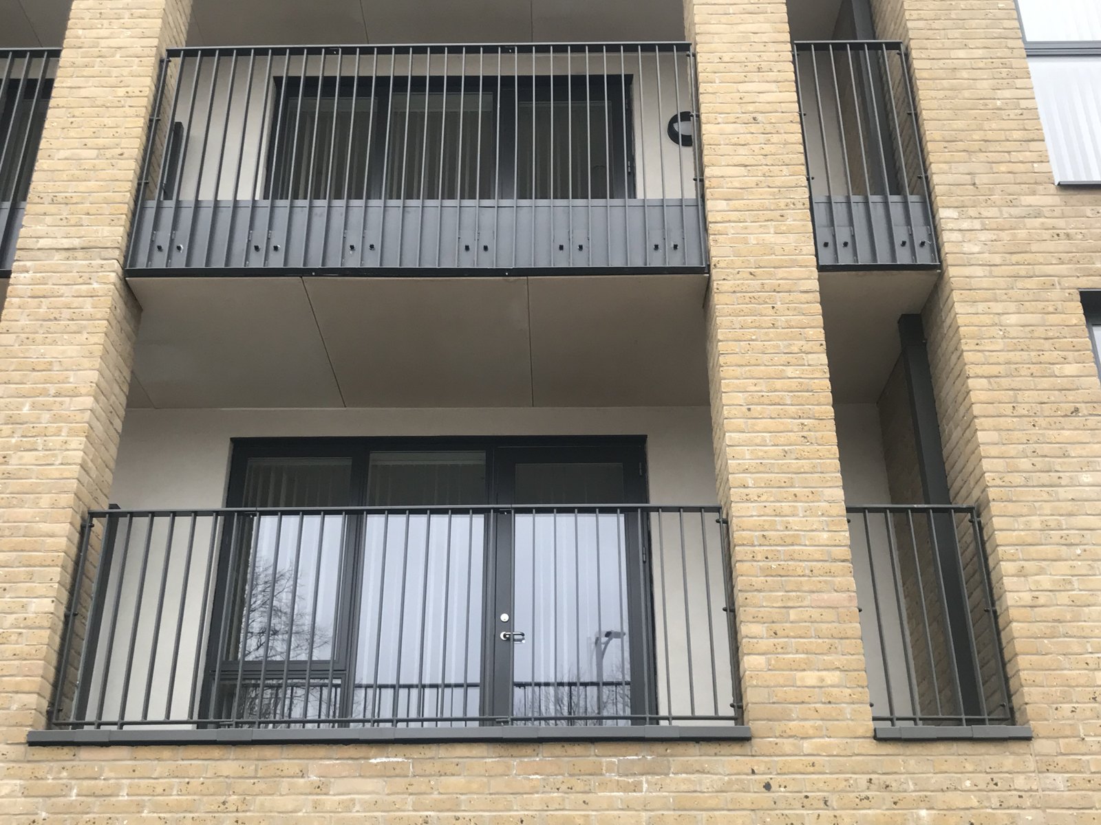 Two storeys of stock brick flats: balcony guarding in anthracite upright bar
