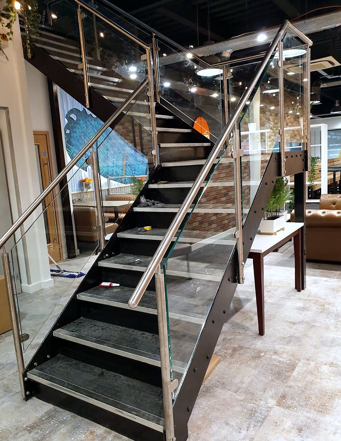 Dark steel stair in a commercial interior, edged with frameless glass under a stainless rail
