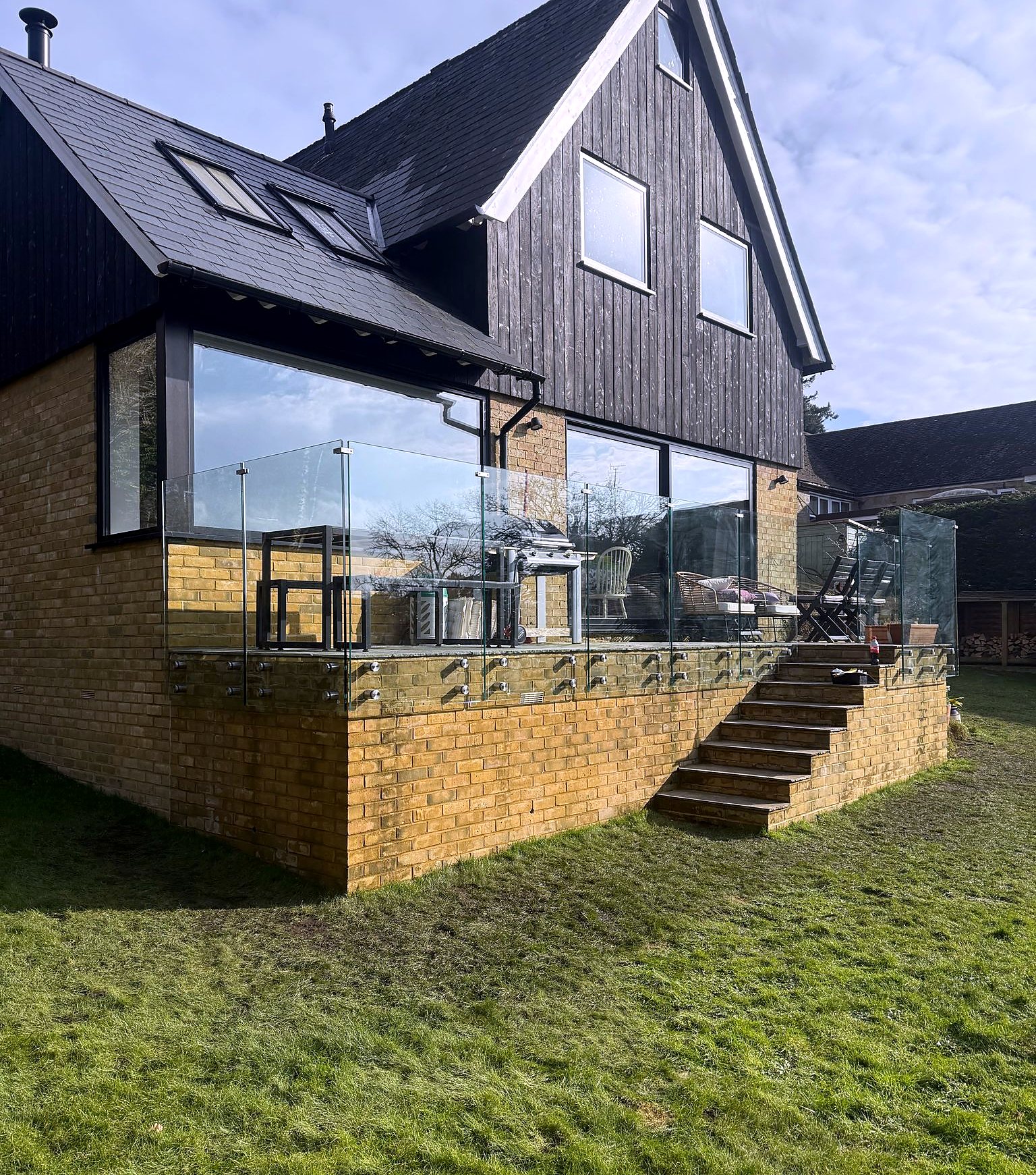 Raised terrace with frameless glass balustrade and garden steps behind a dark-clad house