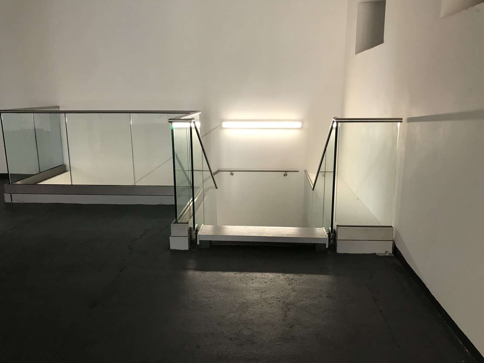 Empty white room: channel-set glass round a stair opening, slim stainless capping rail