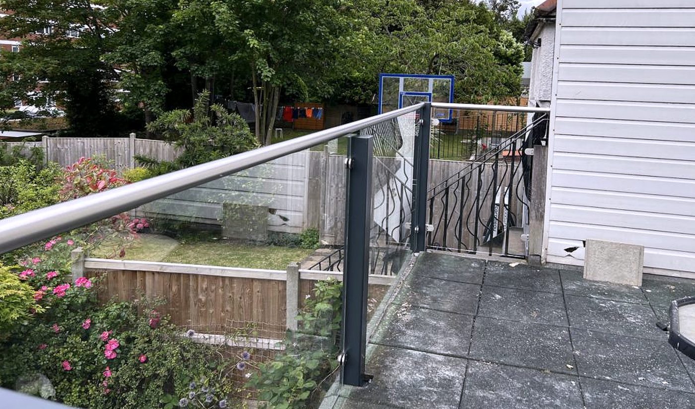 Paved terrace edged in clear glass on a grey square post, stainless rail along the top
