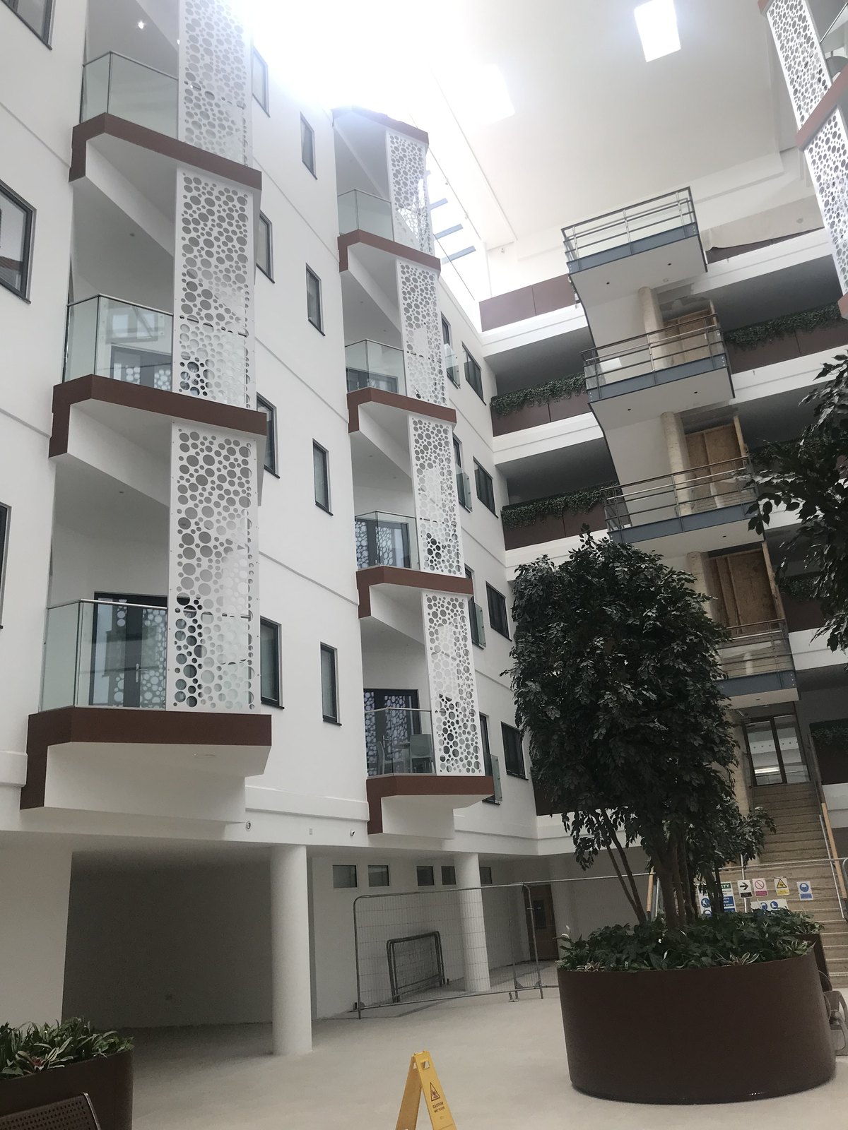 Apartment atrium: glass-fronted walkways and white punched-sheet screens round a tree