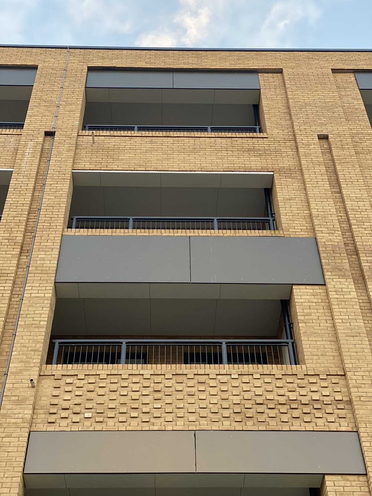 Seen from the street: inset balconies on buff brick flats with grey bar guarding