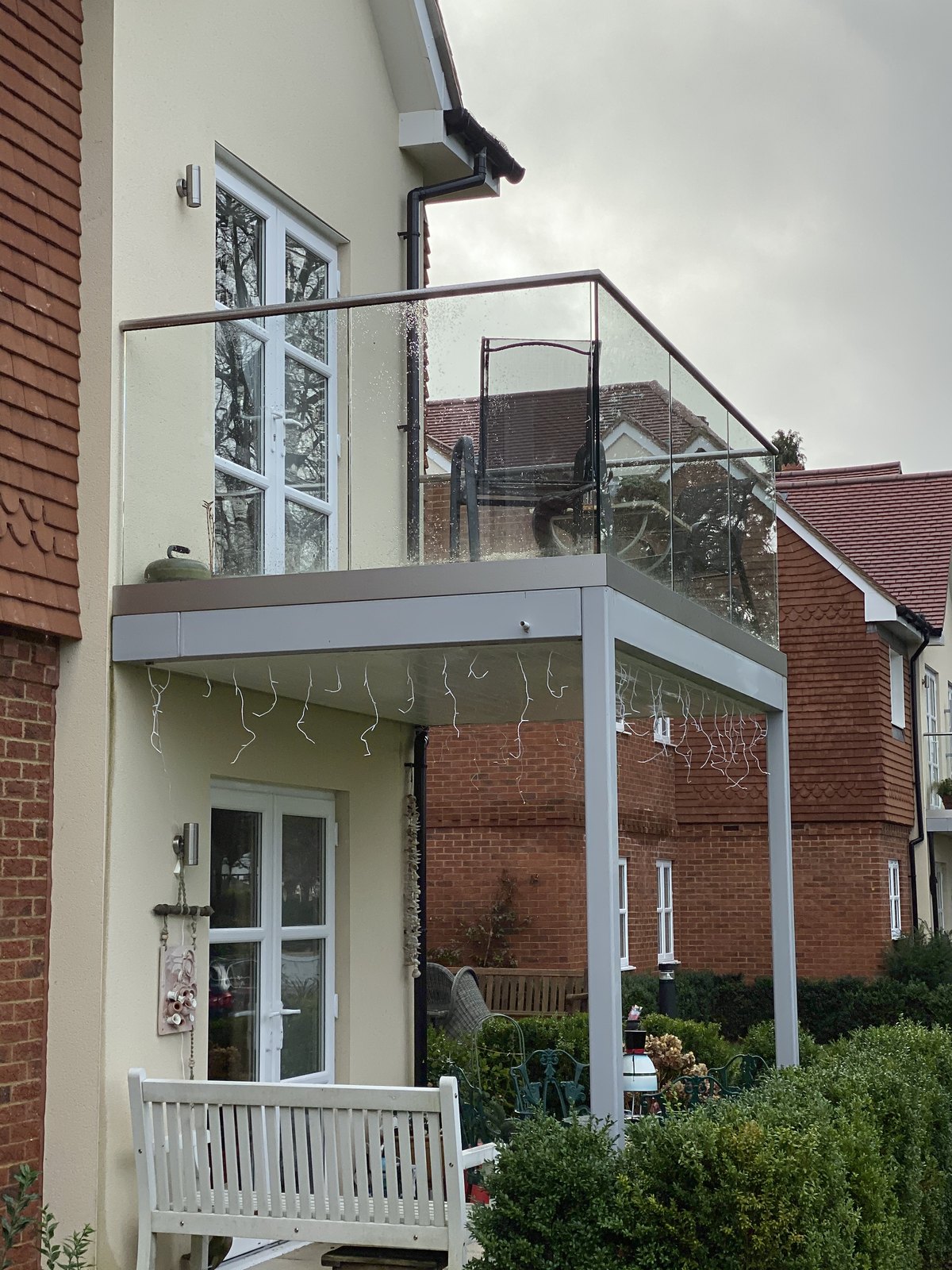 Cream rendered house: post-supported balcony, grey frame, clear glass all round