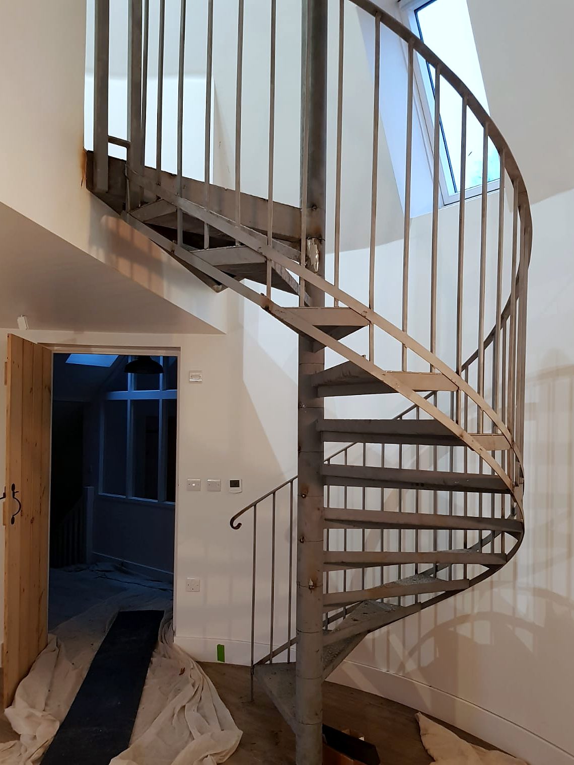 Grey steel spiral stair with vertical bar infill in a round room, dust sheets on the floor