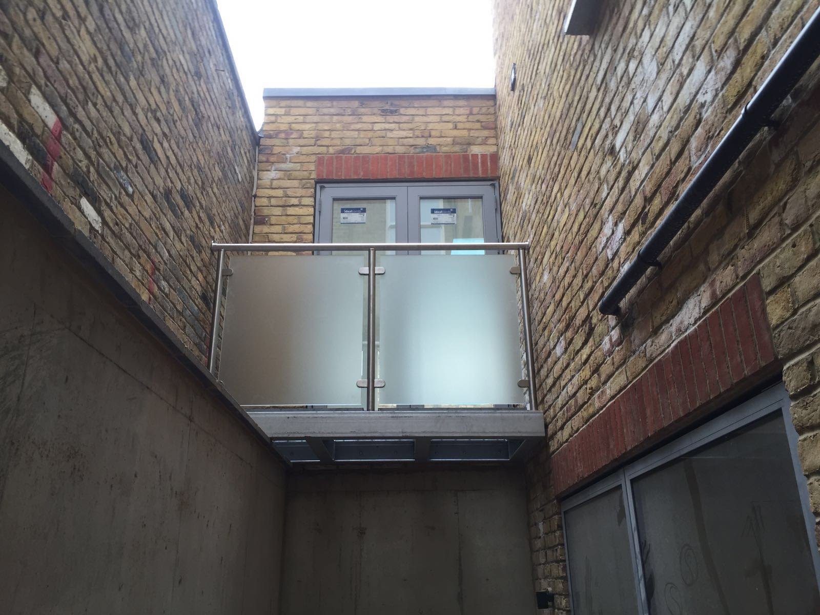 Compact balcony on yellow brick: obscured glass panes between stainless uprights
