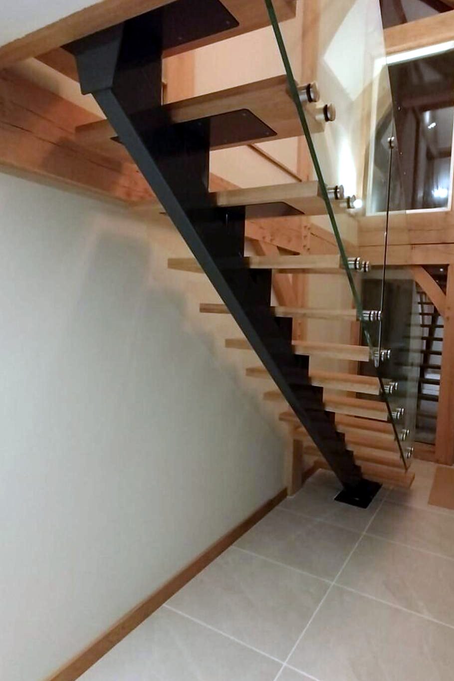 Black steel spine stair with open oak treads and frameless glass guarding, the kind of feature stair Part K stair regulations apply to